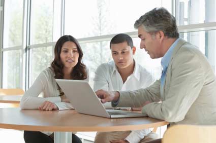 Mature financial advisor explaining an investment scheme on laptop to young multiethnic couple. Horizontal shot.